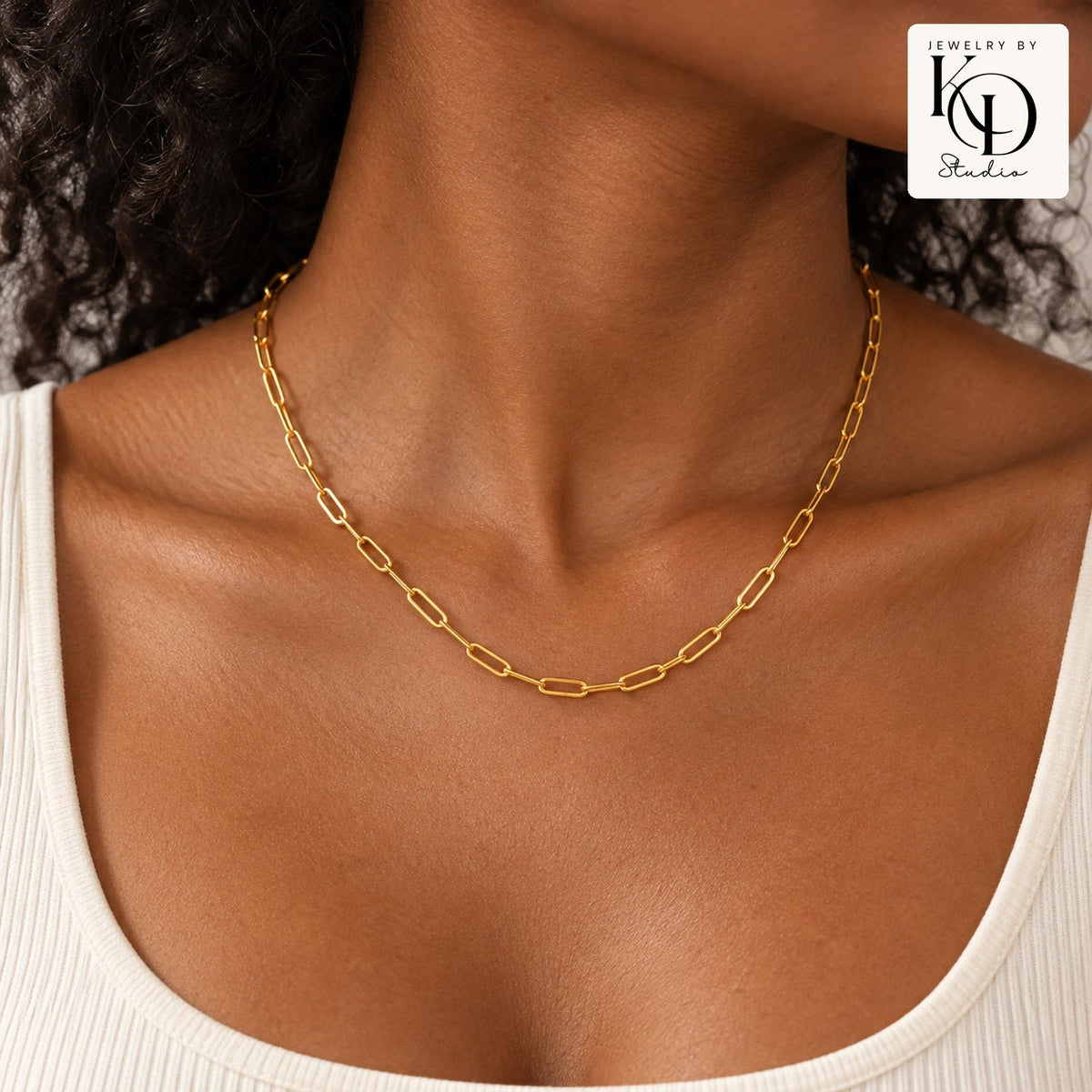 Gold paperclip necklace modeled by a Black woman, approved stacked KD Studio logo