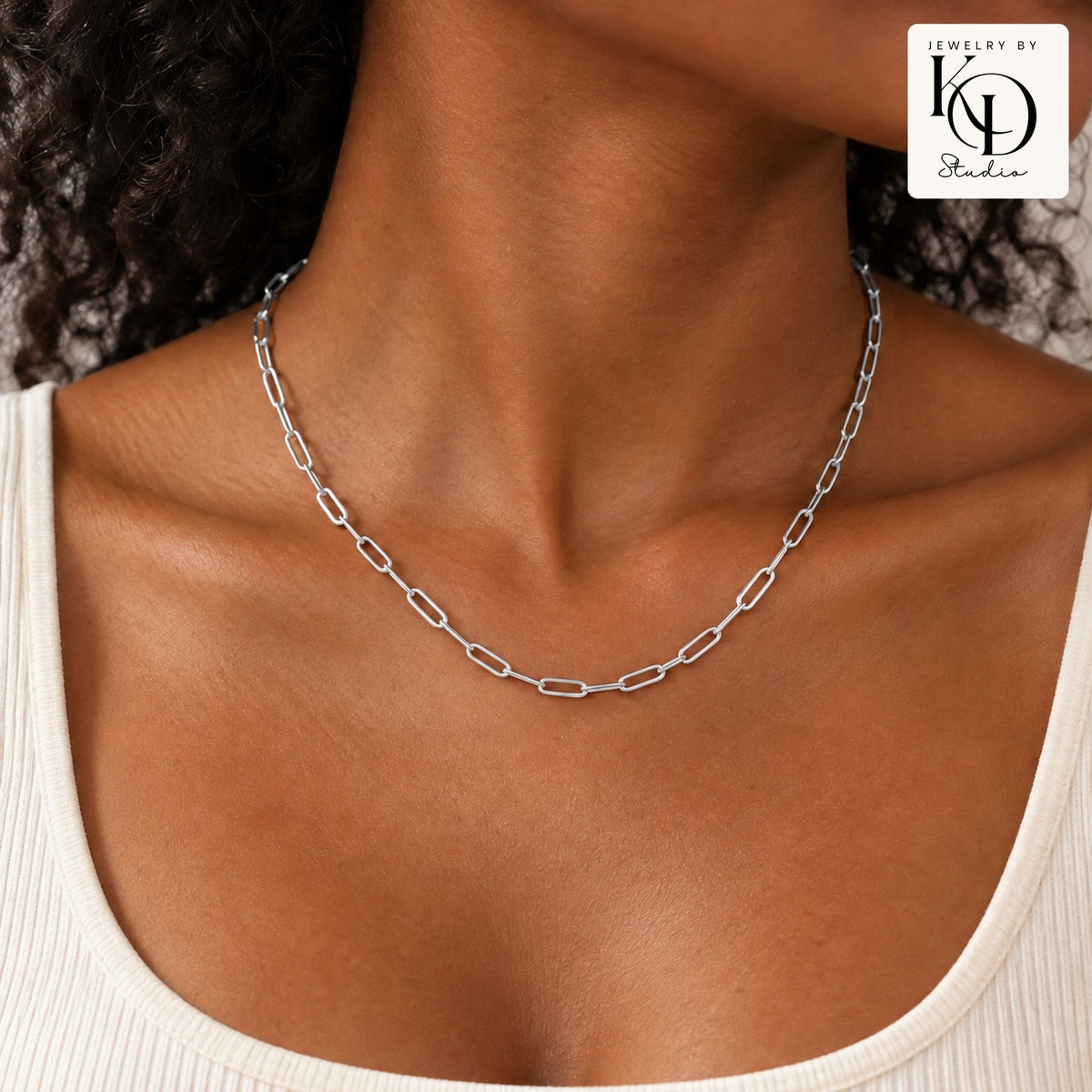 Silver paperclip necklace modeled by a Black woman, approved stacked KD Studio logo